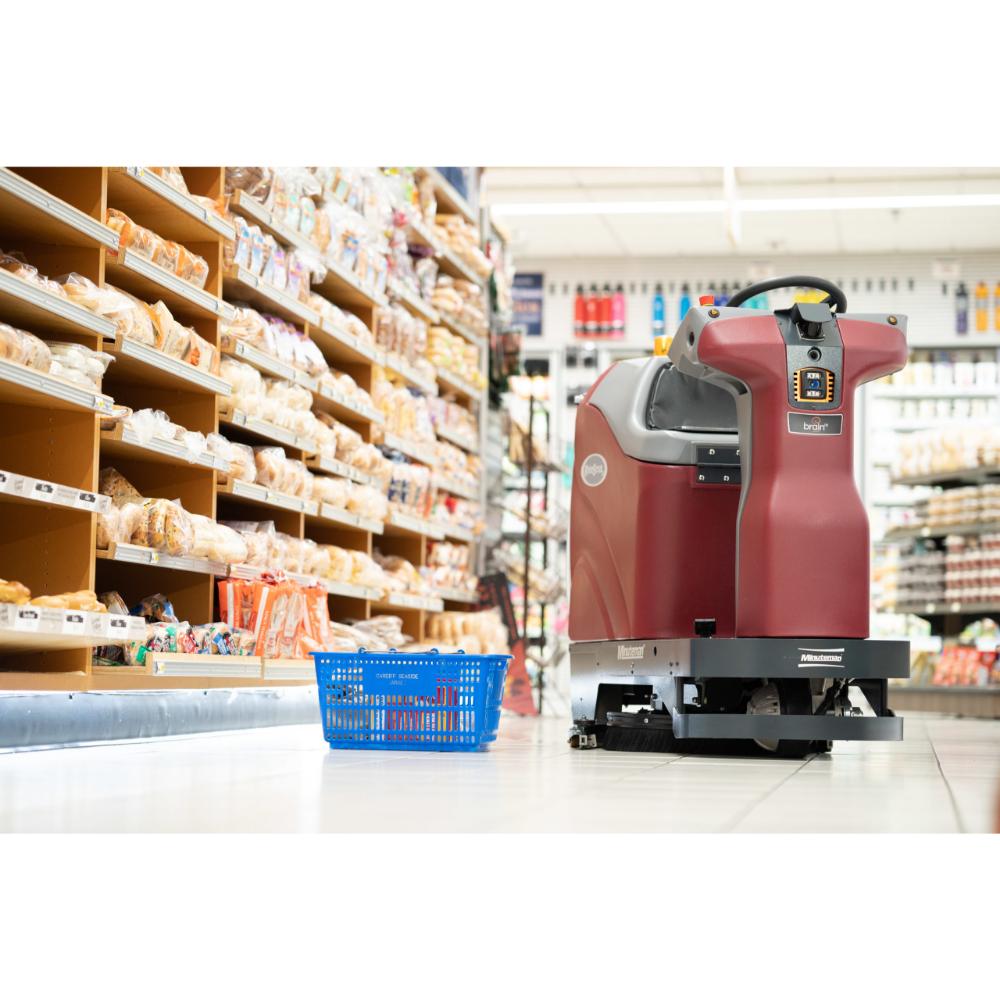 Minute man Roboscrub autonomous scrubber in the bread isle of a grocery store with a blue grocery basket lying next to it in the isle.