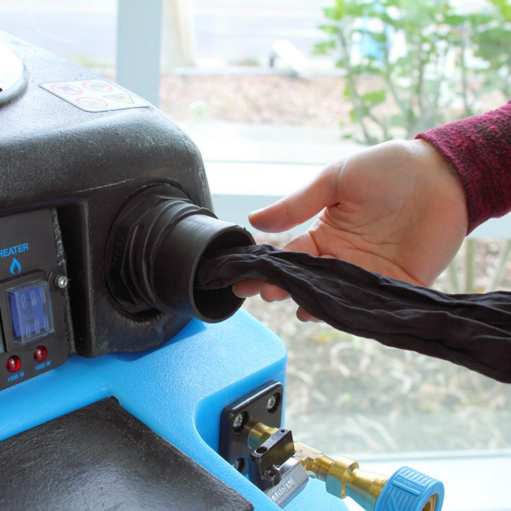 Person using a machine to stretch a black fabric, with a blurred outdoor background