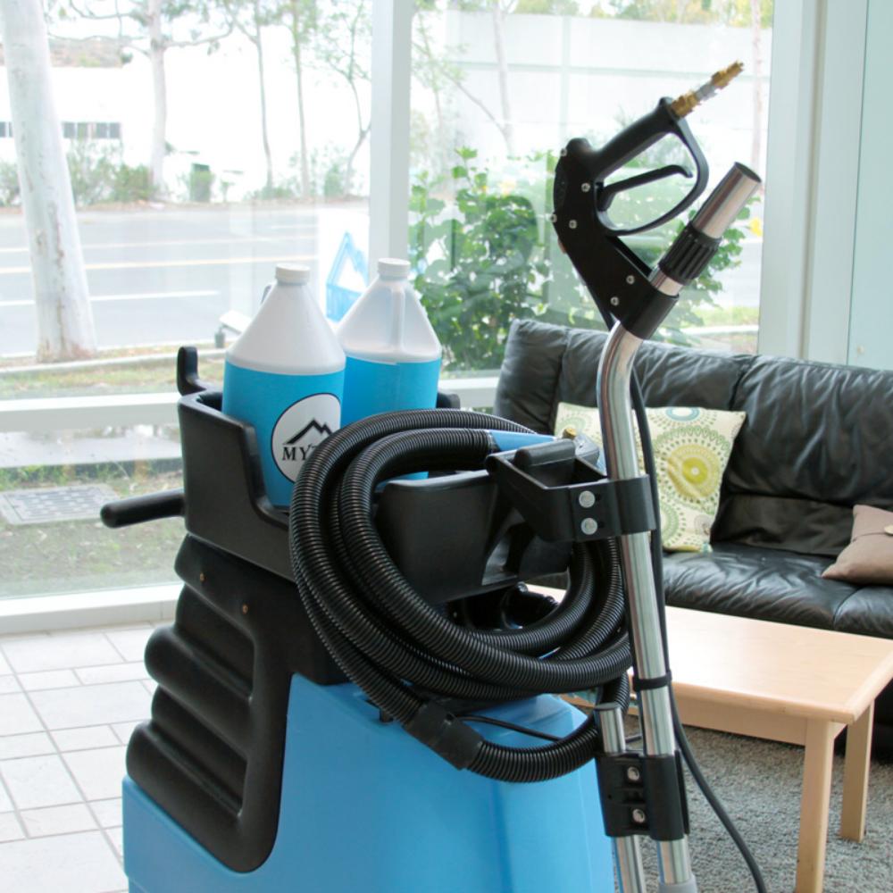 Blue pressure washer with a nozzle and hoses in a room with a couch and window.