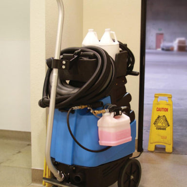 Blue cleaning machine with hoses and bottles in a room with a wet floor sign.
