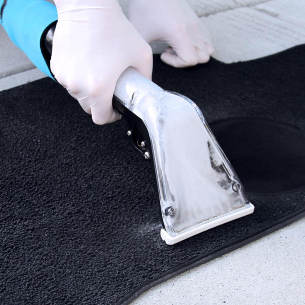 Person cleaning a black car mat with a Mytee S 300h Tool, wearing gloves.