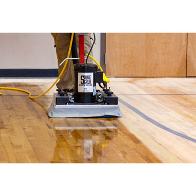 Floor cleaning machine on a wooden floor with a person operating it.