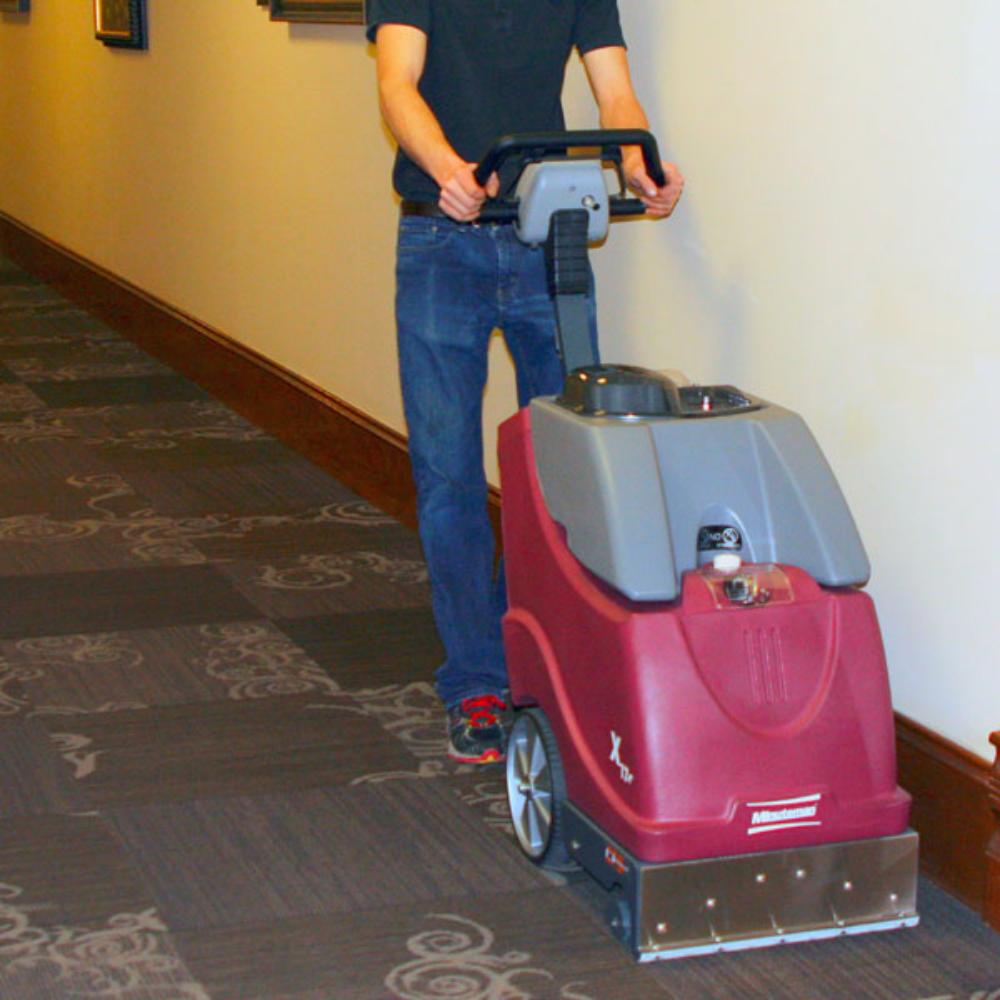 Man pushing a x-17 carpet cleaner down a carpeted hotel hallway 