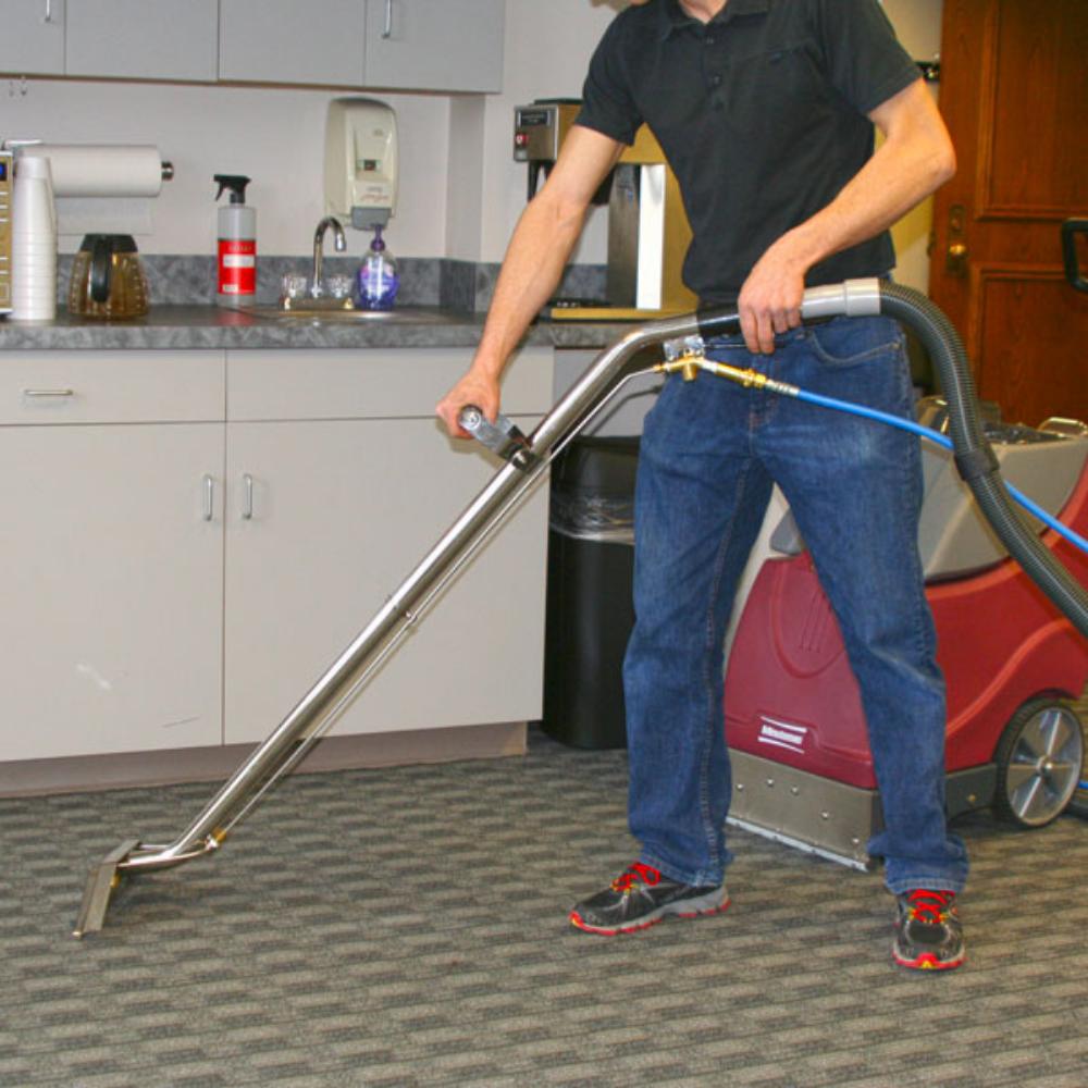 Man using stainless steel carpet cleaning vacuum attachment on carpet in an office breakroom